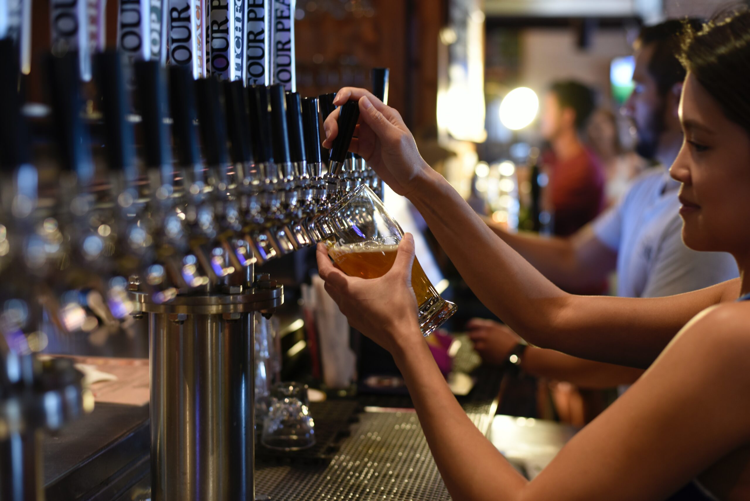 woman pouring a beer behind the bar | sports bars Highlands Ranch