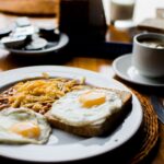 a plate with toast, eggs, and hash browns with a cup of coffee and other assorted breakfast items | breakfast
