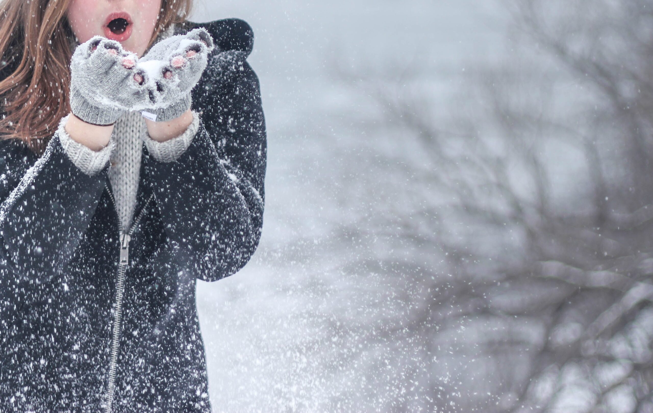 woman dressed in winter gear blowing snowflakes outdoors | winter activities Highlands Ranch